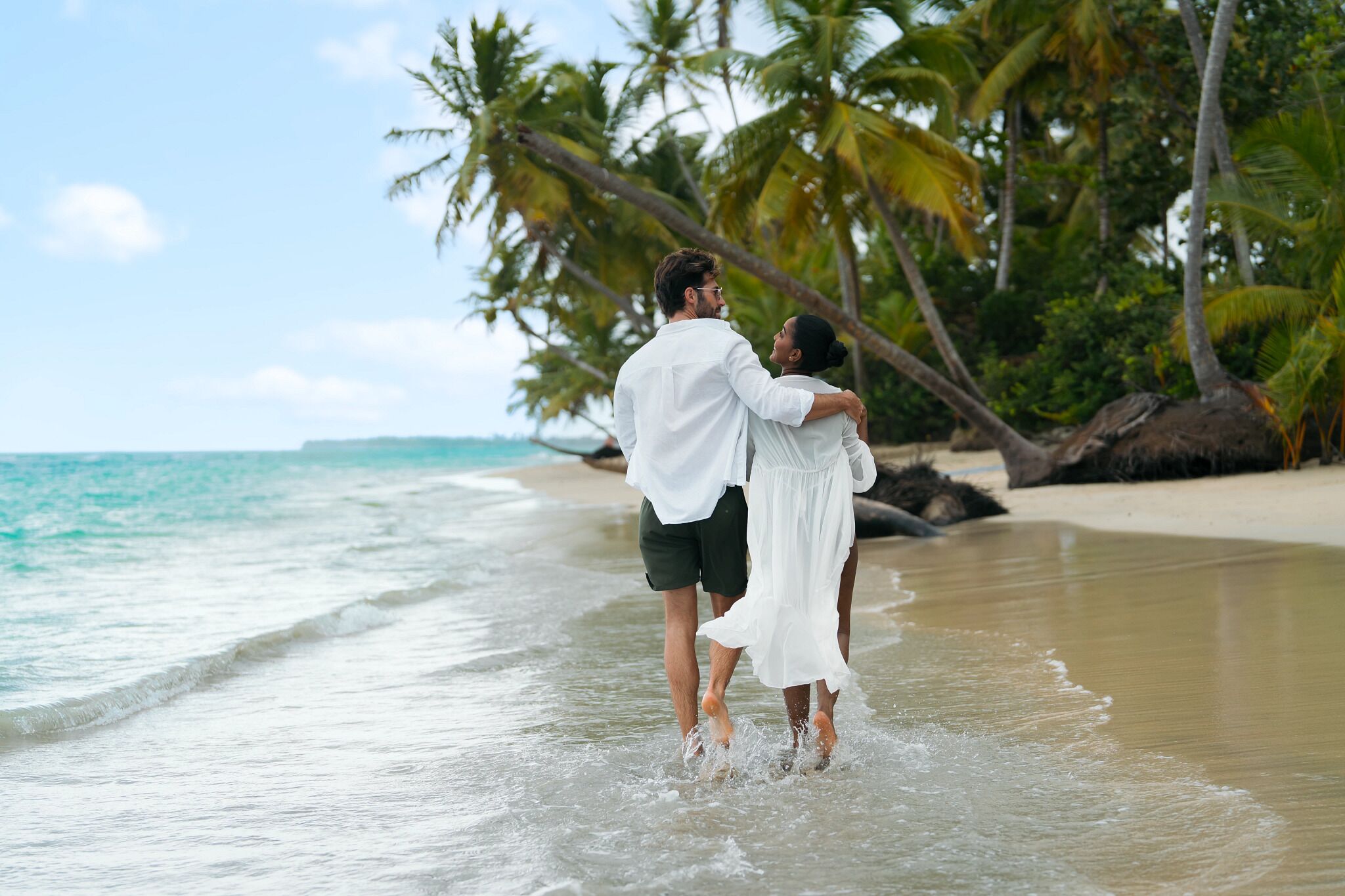 A couple embracing on a beach with palm trees and ocean in the background.