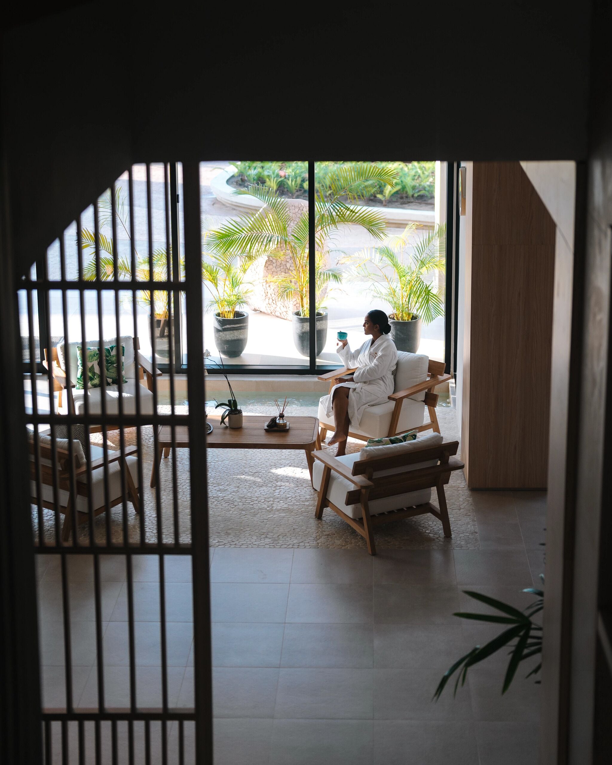 A room with a large window, a wooden chair, a small table, and potted plants.