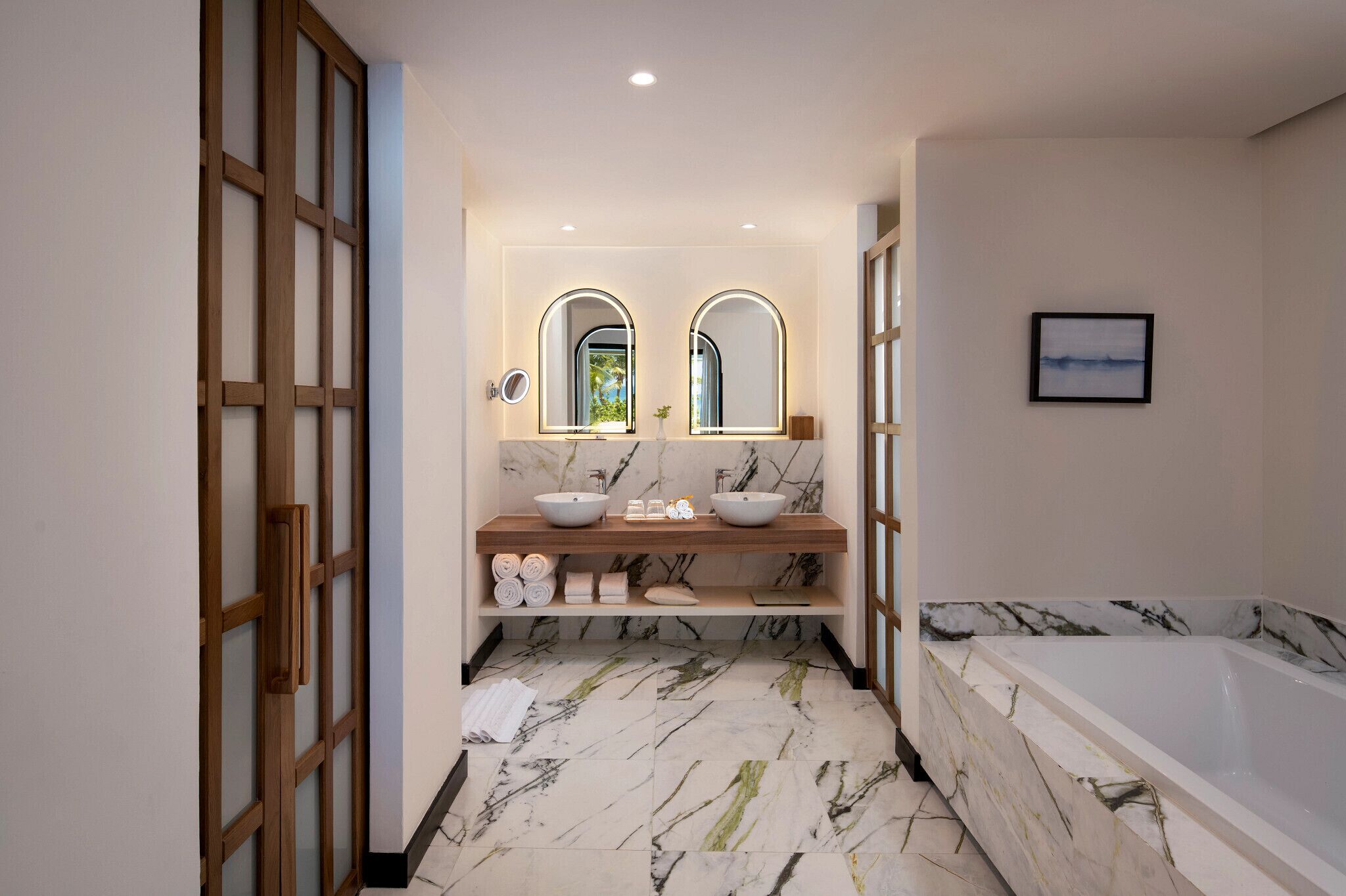 Ein modernes Badezimmer mit Marmorboden, zwei Waschbecken, einer großen Badewanne und einer Holztür.