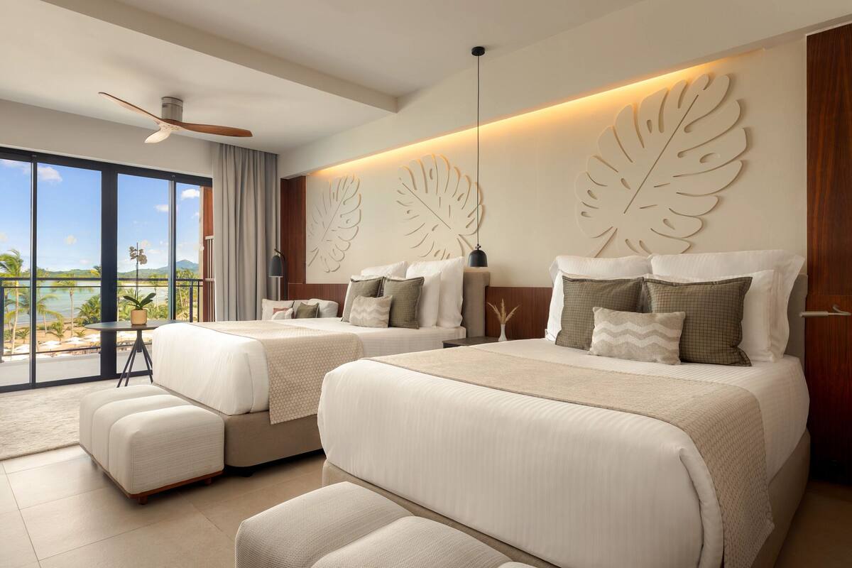 A hotel room with two beds, a balcony with a view, and a ceiling fan.