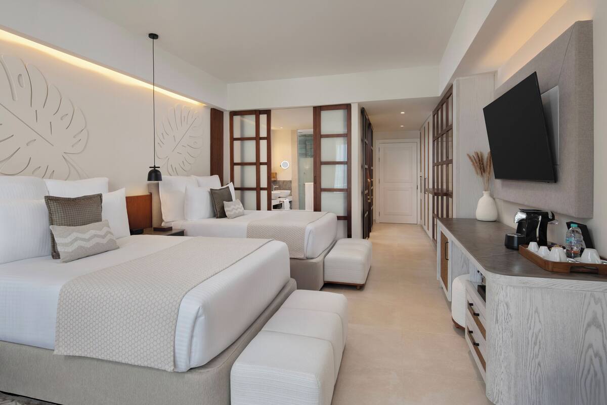 A modern hotel room with two beds, a desk, and a TV.