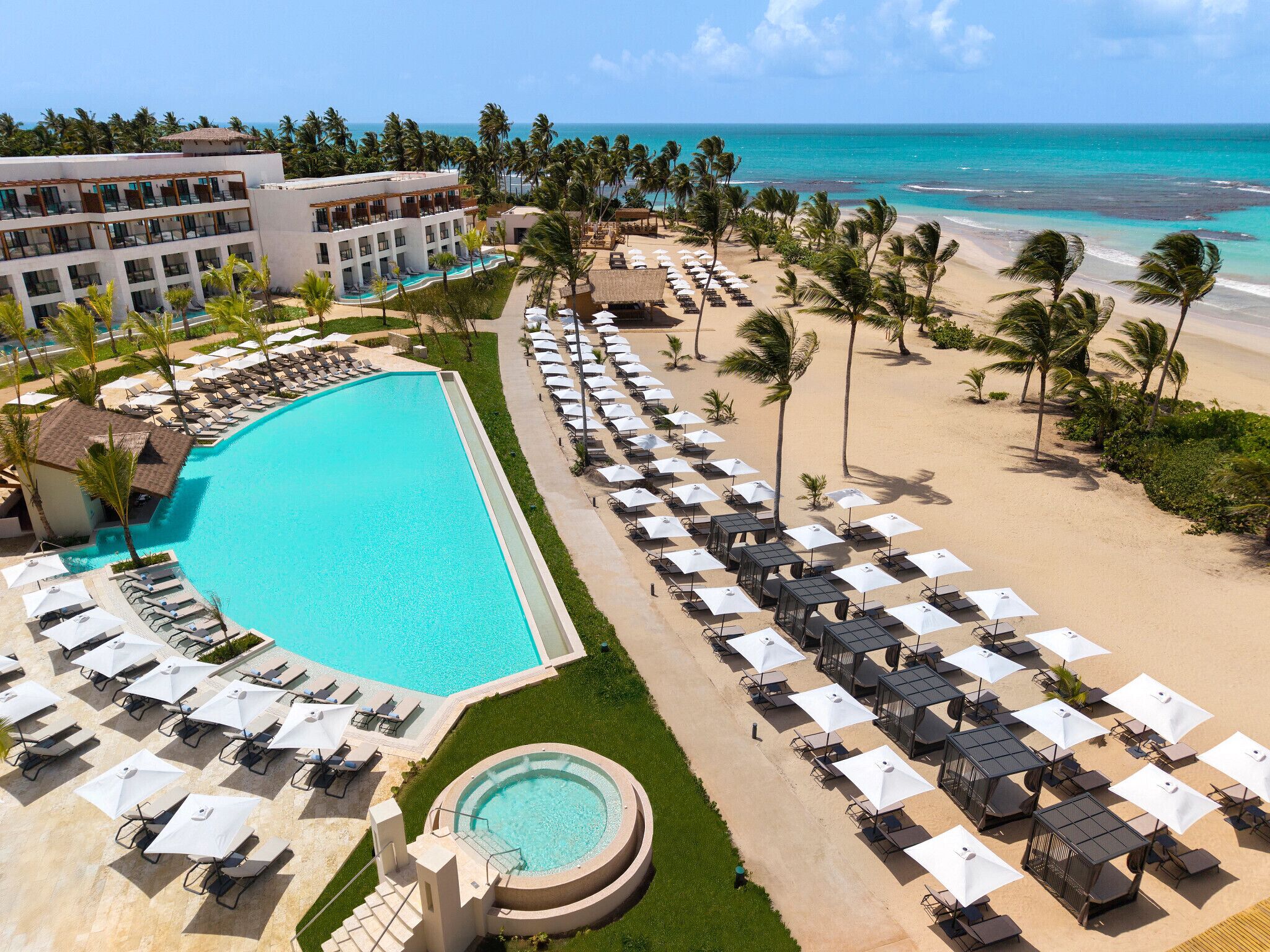 Un resort con una piscina grande, sillas de descanso en la playa y vistas al océano.