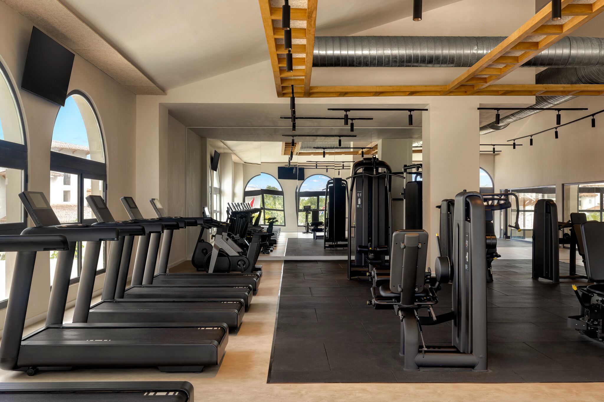 A gym with treadmills, weight machines, and a ceiling with exposed beams and ductwork.