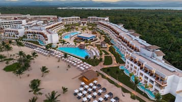 A resort with multiple swimming pools, a beach area, and a mountainous backdrop.
