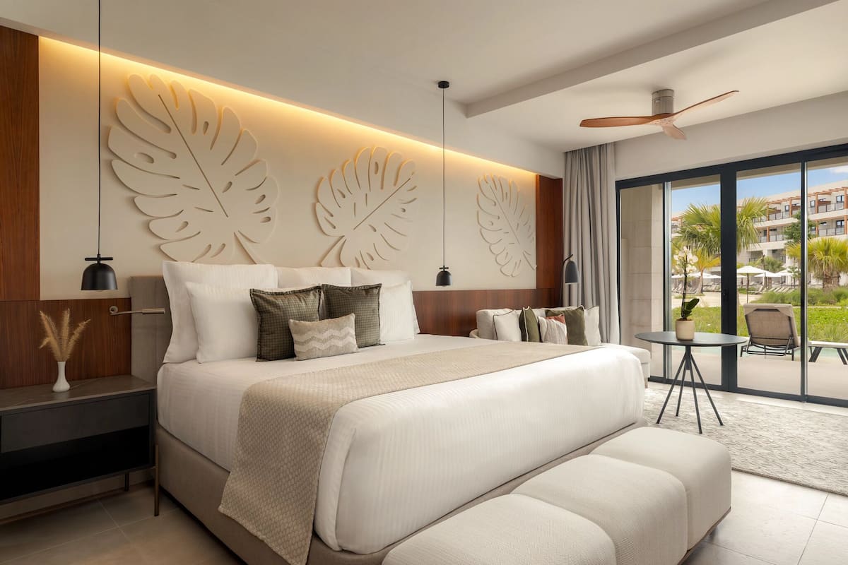 A modern hotel room with a large bed, a ceiling fan, and a view of the outdoors.