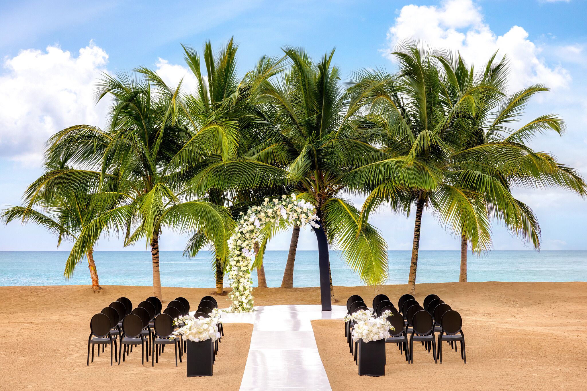 A beach wedding setup with chairs and a white aisle.