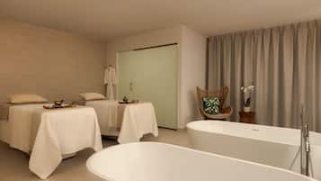 A modern spa room with two massage tables, a large bathtub, and a wicker chair.