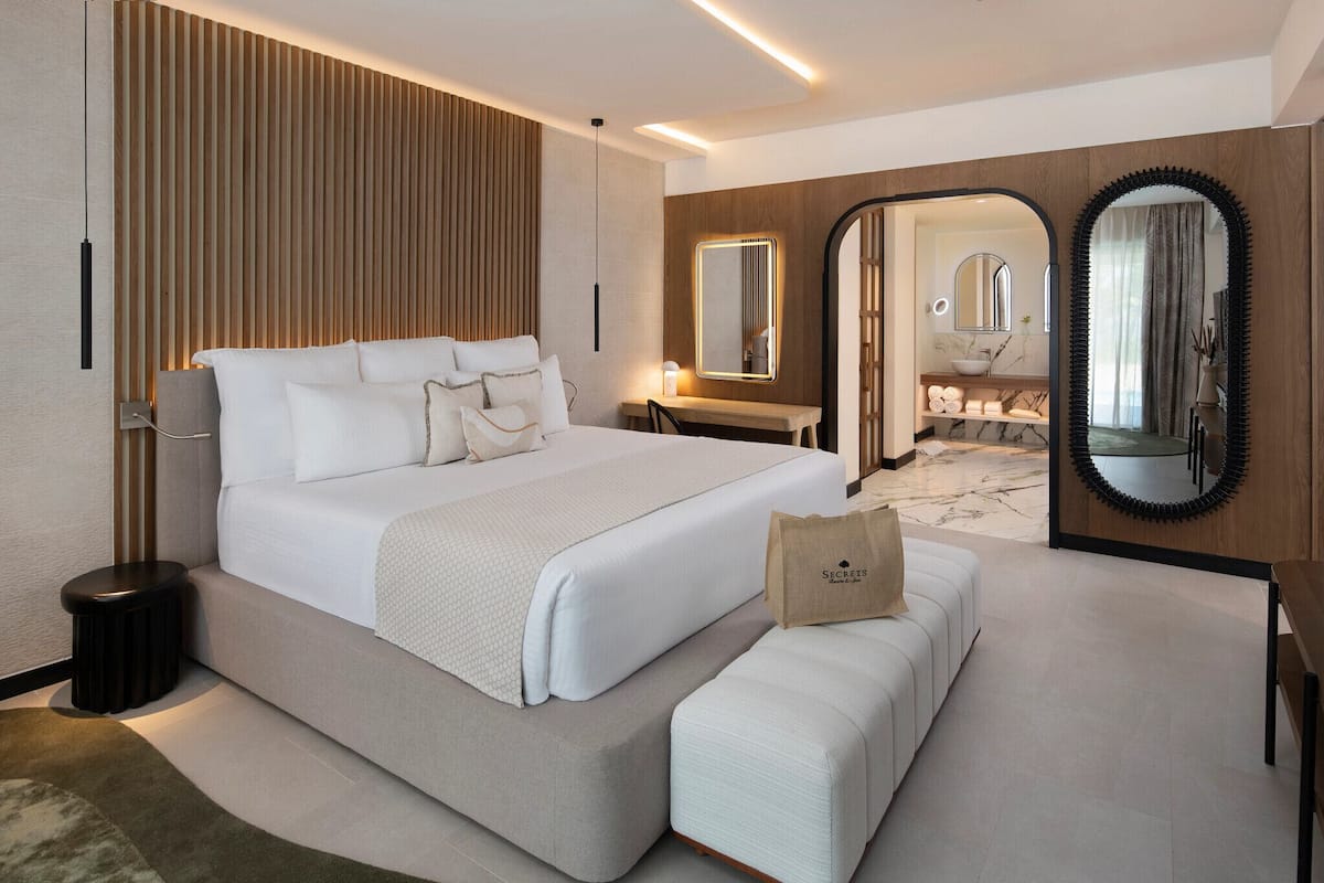 A modern hotel room with a large bed, a vanity with a mirror, and a bathroom visible through an archway.