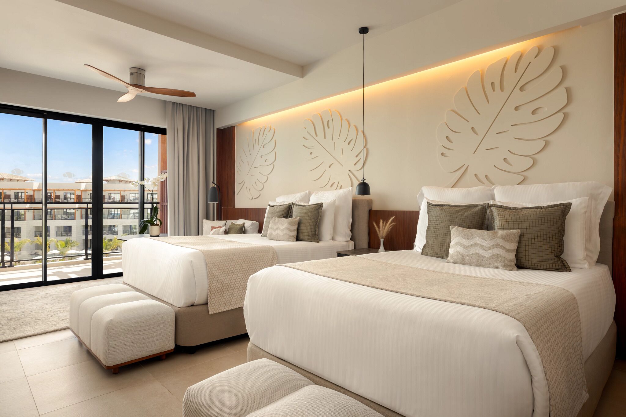 A modern hotel room with two beds, a ceiling fan, large windows, and a city view.