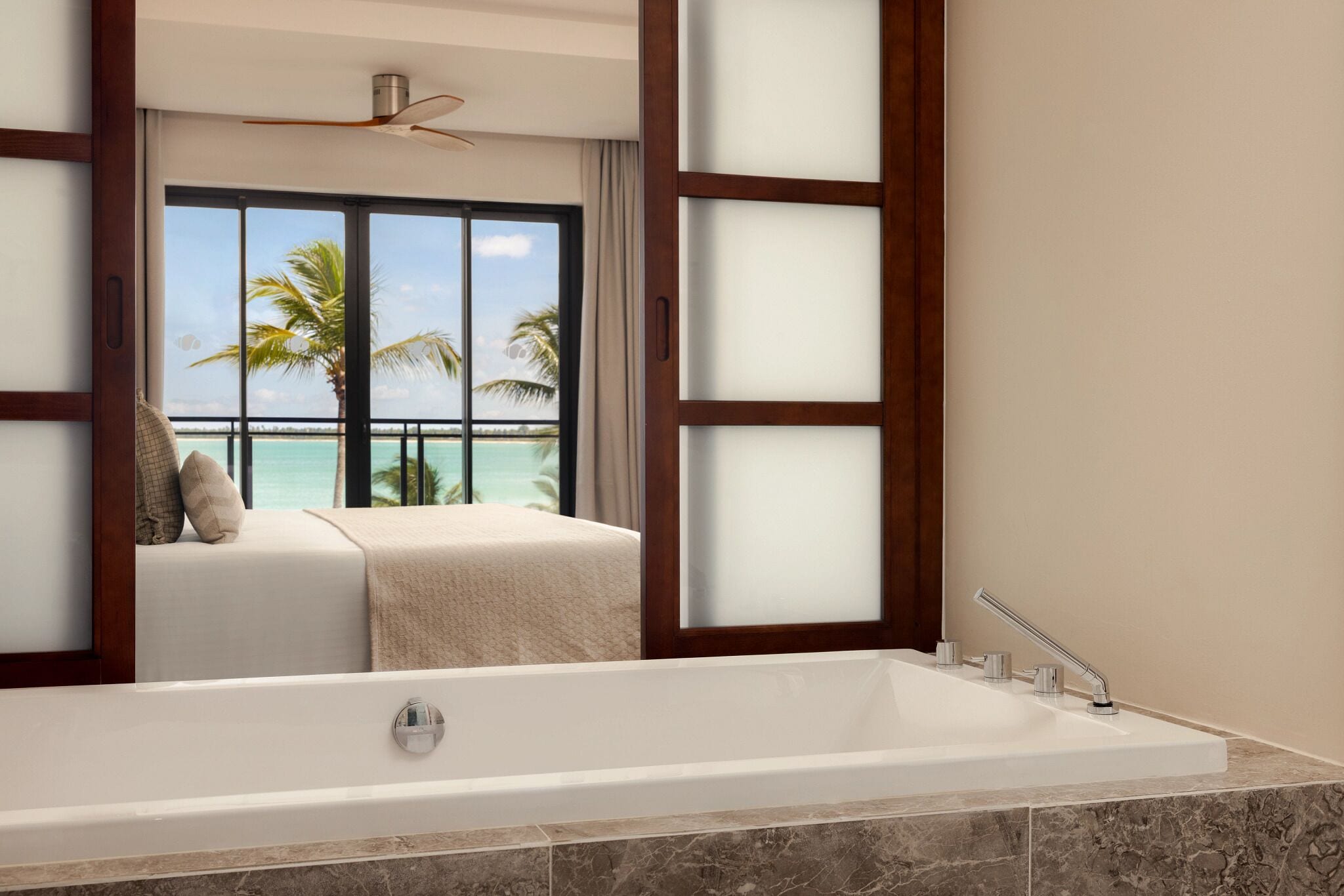 A bathroom with a large bathtub, a ceiling fan, and a view of the ocean through a window.