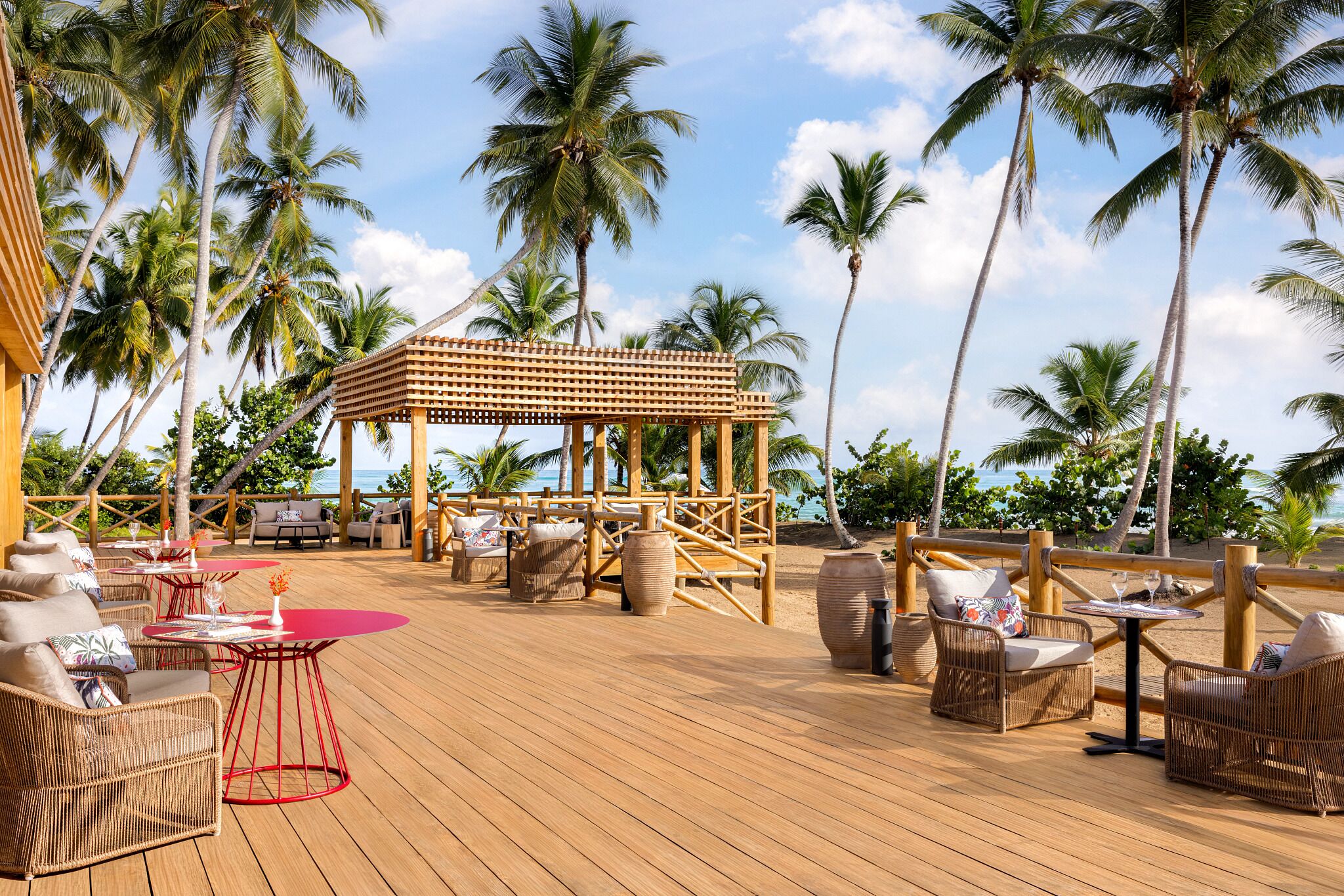 A wooden deck with wicker furniture, a wooden gazebo, and palm trees.