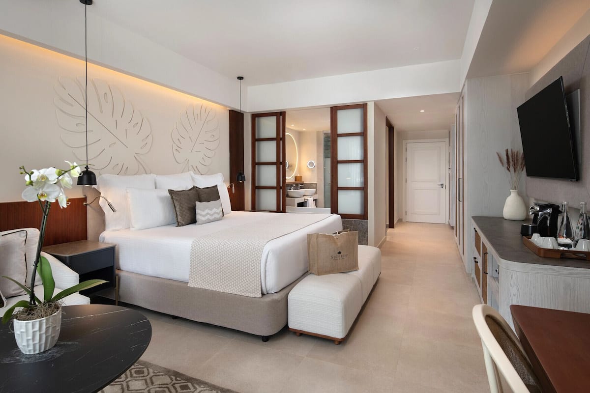 A modern hotel room with a large bed, a desk, a TV, and a bathroom visible through an open door.