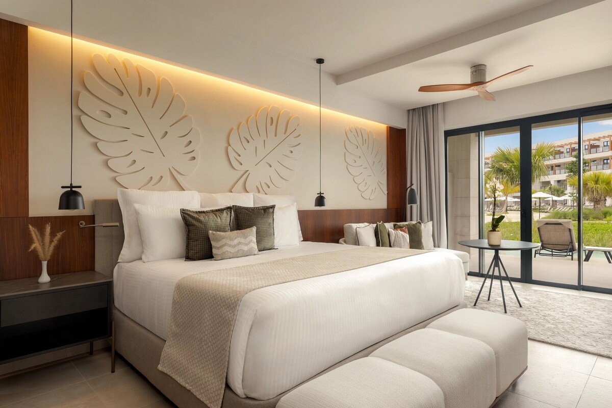 A modern hotel room with a large bed, a ceiling fan, and a view of the outdoors.