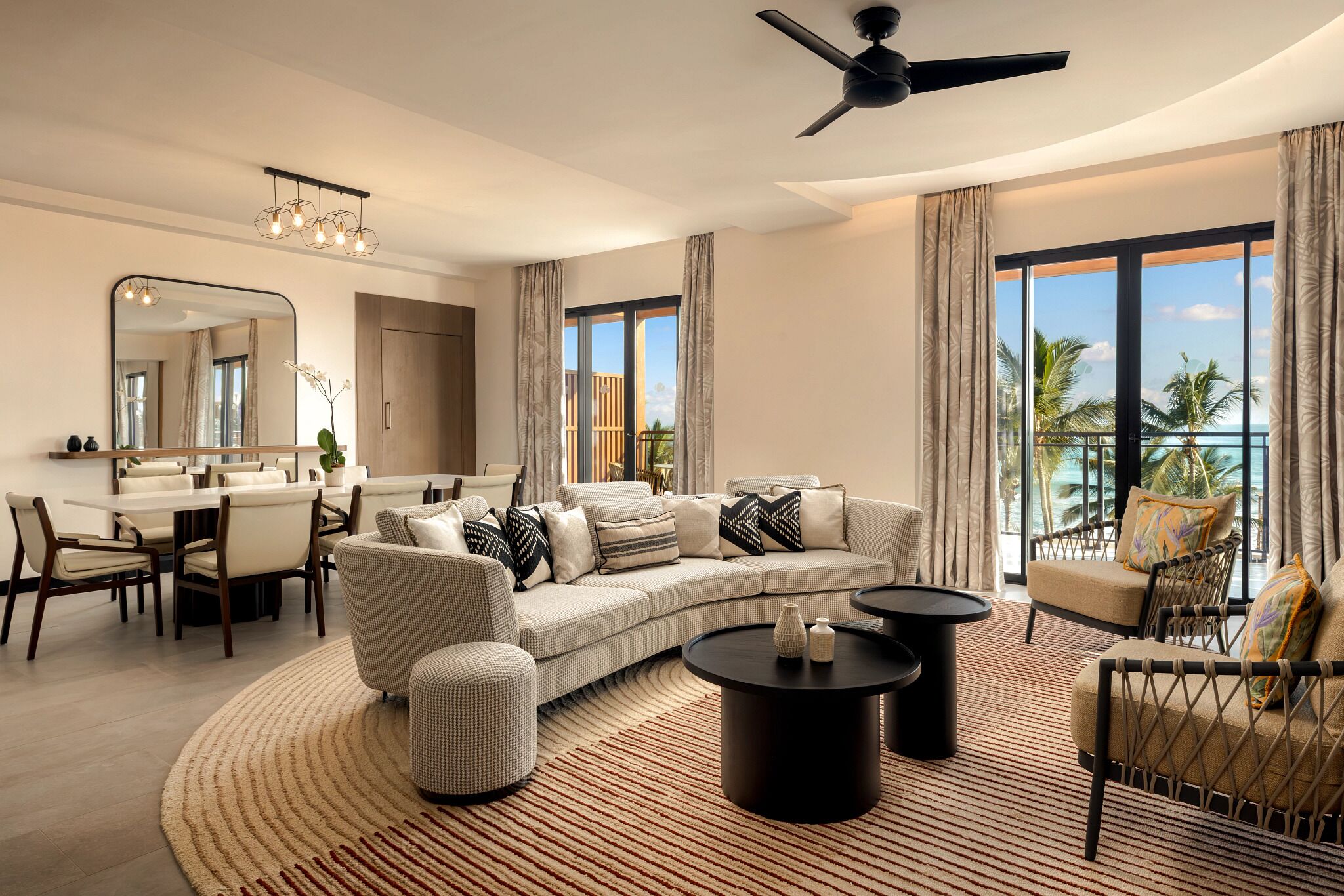 A modern living room with a sofa, coffee table, and chairs, a dining area with a table and chairs, and large windows with a view.