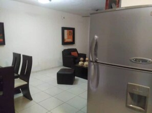 Cozy living space with a stainless steel refrigerator, black sofa, and two chairs.