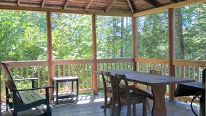 A covered outdoor seating area with a wooden table and chairs, a bench, and a small table. - 1 Bedroom Riverside Cabin in The Forks, ME (The Forks)