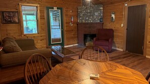 A cozy cabin interior with a wooden dining table, a cushioned sofa, a fireplace, and a stone accent wall. - Riverside Cabin in The Forks (The Forks)