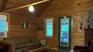A cozy cabin interior with wooden walls, a green door, a fireplace, and a wooden floor. - Riverside Cabin in The Forks (The Forks)