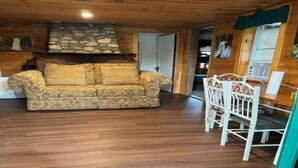 A cozy living room with a patterned sofa, a stone fireplace, and a white dining set. - 2 Bedroom Riverside Cabin (The Forks)