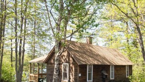 A rustic cabin with a porch, surrounded by trees. - 2 Bedroom Riverside Cabin (The Forks)