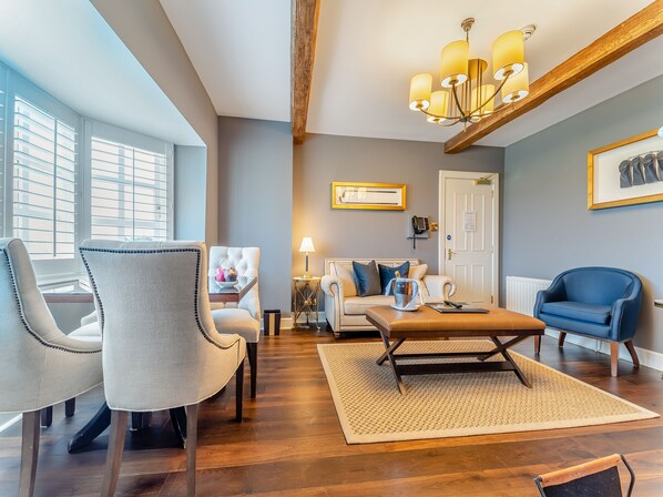 Un salon moderne avec une poutre en bois au plafond, un lustre, un canapé blanc, un fauteuil bleu et une table basse.