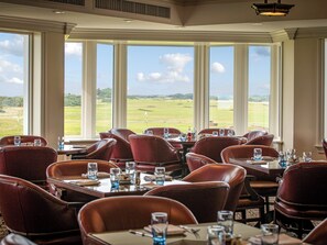 Un restaurant avec des chaises et des tables en cuir, de grandes fenêtres donnant sur un terrain de golf.