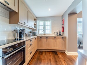 A modern kitchen with wooden cabinets, a built-in oven, and a window providing natural light. - Royal Aberdeen - UKC6917 (Turnberry)
