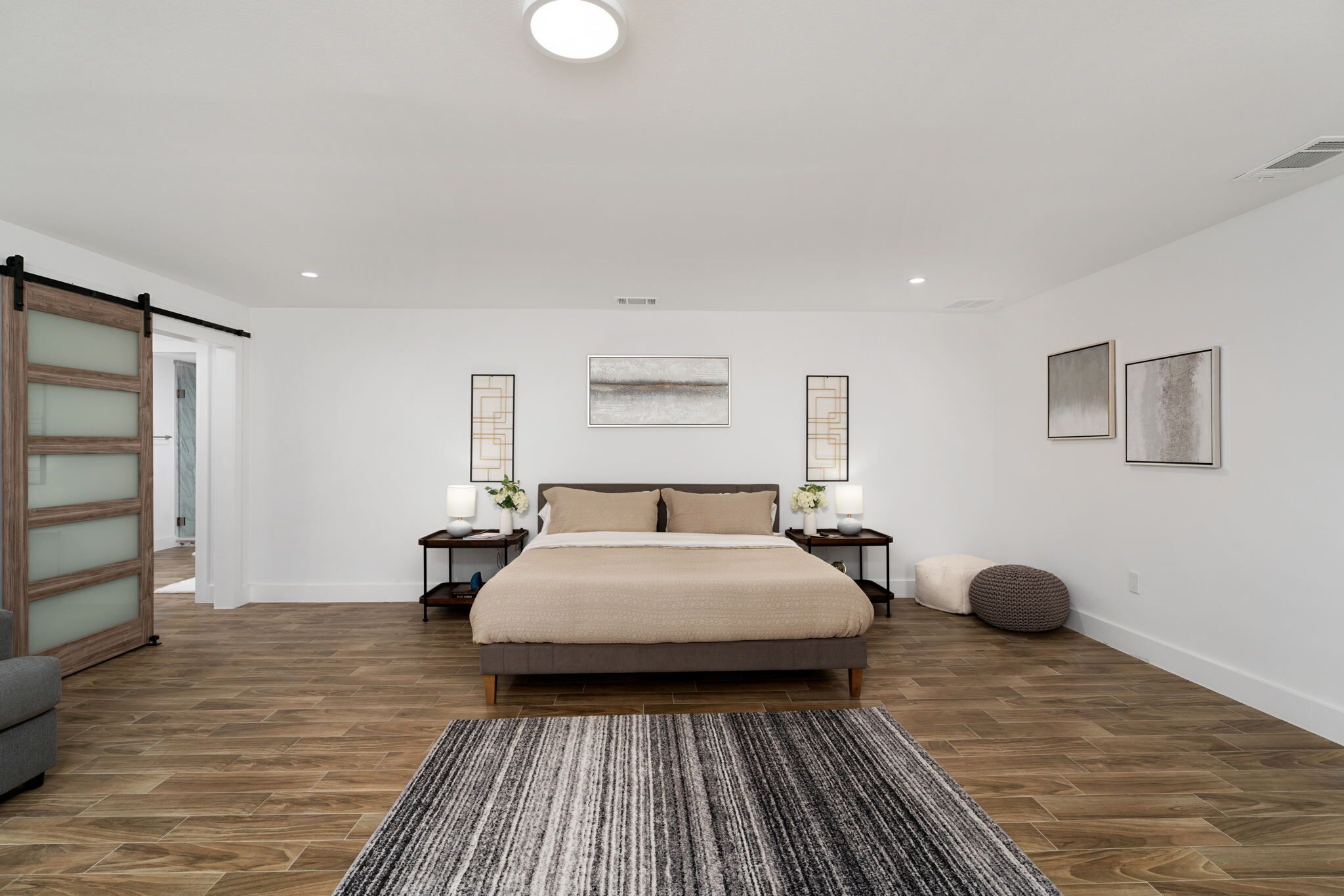 A bedroom with a large bed, wooden flooring, a gray striped rug, and two bedside tables with lamps.