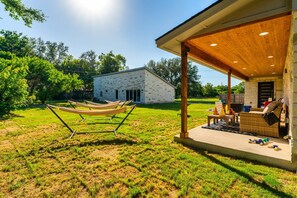 A covered patio area with outdoor furniture, a hammock, and a stone building in the background. - The Gateway 6BED 2 Houses GameRoom Pool (Cedar Park)