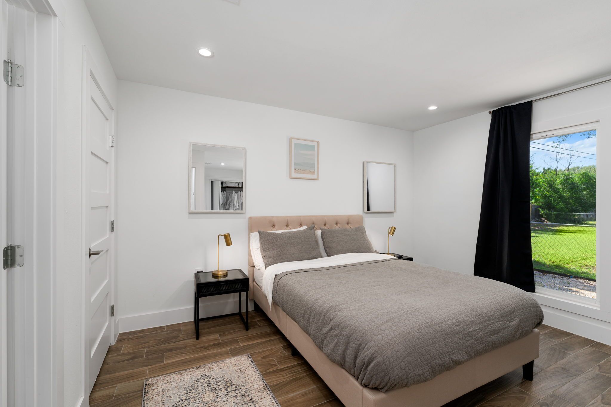 Un dormitorio con cama, mesitas de noche, un espejo y una ventana con vistas a zonas verdes.