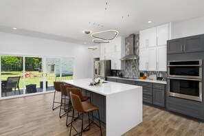 Una cocina moderna con una isla grande, taburetes de bar, electrodomésticos de acero inoxidable y vistas al exterior.