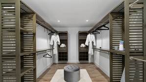 Un armario vestidor con estantes de madera, colgadores para abrigos y un otoman central.