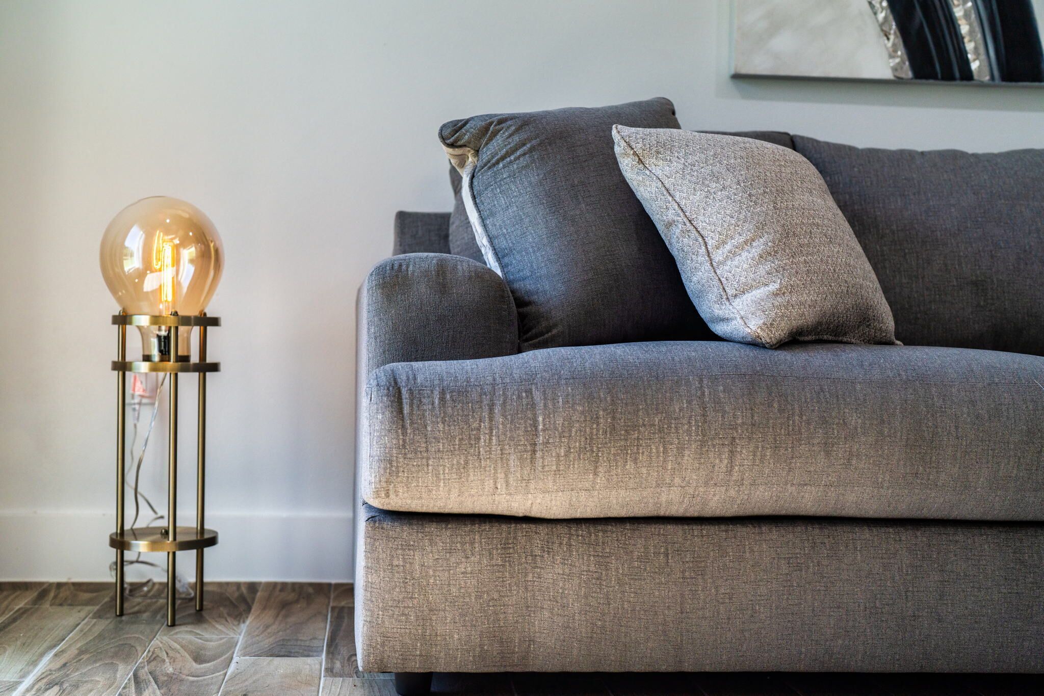 Un salon moderne avec un canapé gris, une lampe de table ronde et une œuvre d’art accrochée au mur.