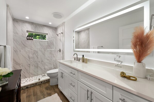 Un baño moderno con pared de ducha de mármol, un espejo grande y un mueble de tocador con cajones.