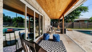 Un patio techado con piscina, mobiliario exterior y un muro de piedra.