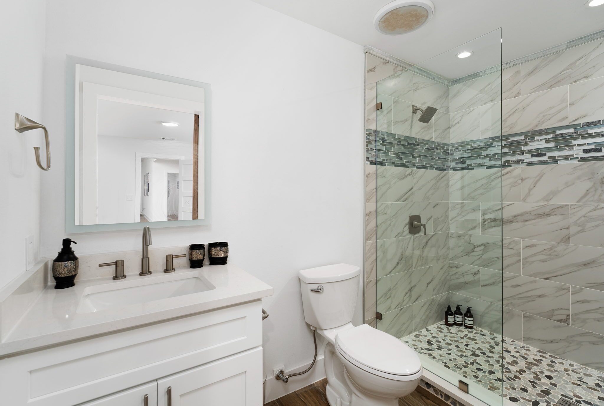 Un baño moderno con lavamanos blanco, un espejo, inodoro y cabina de ducha con mampara de vidrio.