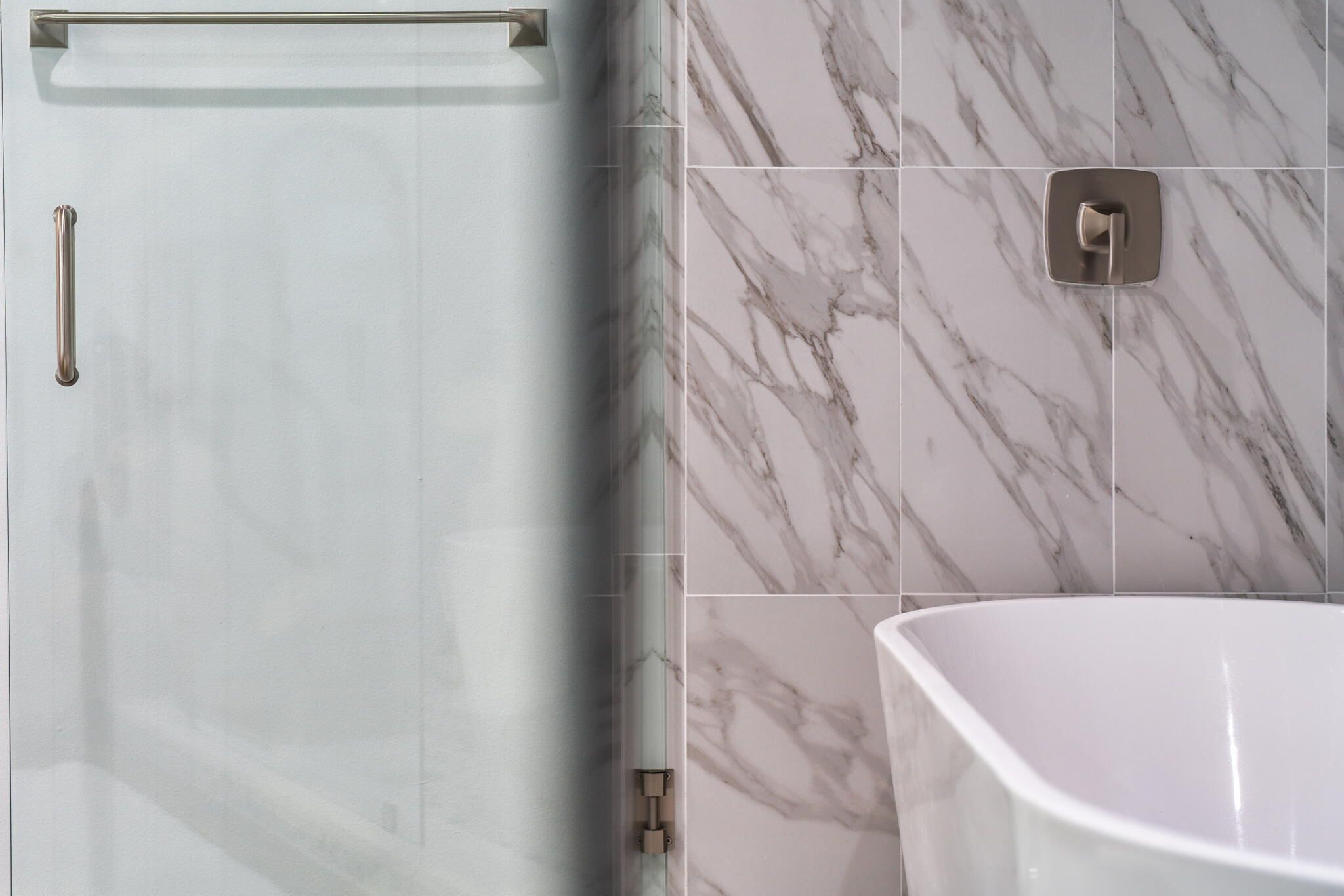 Un baño con cabina de ducha de vidrio, bañera blanca y paredes con diseño de mármol.