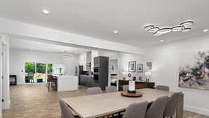 Una cocina moderna con armarios blancos, una isla central y un comedor con mesa y sillas de madera.
