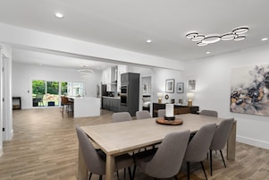 Uma cozinha moderna com armários brancos, uma ilha central e um espaço de jantar com mesa e cadeiras de madeira.