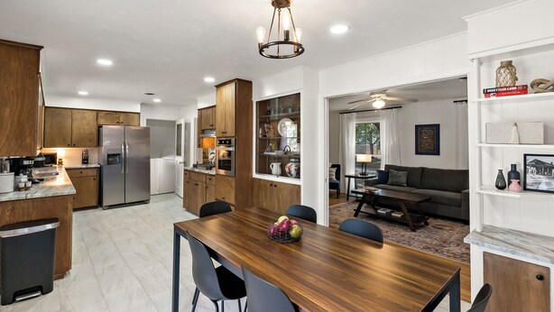 Una cocina moderna con armarios de madera, un refrigerador de acero inoxidable y una zona de comedor con una mesa y sillas de madera.