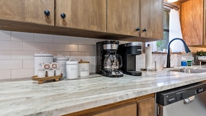 Una cocina con armarios de madera, encimera de mármol, cafetera y recipientes de almacenamiento etiquetados como 'Azúcar', 'Café' y 'Té'.