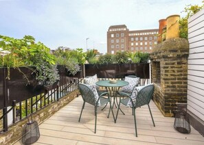A rooftop patio with a table and chairs, surrounded by a black metal fence and lush greenery. - Luxury Shawfield Apartment in London (London)