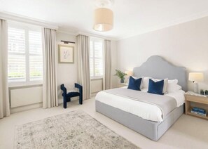 A hotel room with a large bed, a chair, a nightstand, and a window with curtains. - Luxury Shawfield Apartment in London (London)