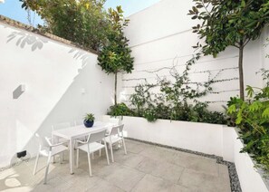 A patio with a white table and chairs, surrounded by greenery and a white wall. - Luxury Shawfield Apartment in London (London)