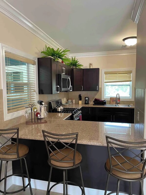 A modern kitchen with dark cabinets, a granite countertop, a built-in microwave, and a gas stove. There are three bar stools with cushioned seats.
