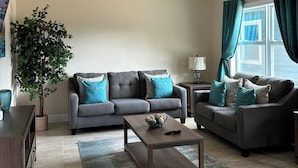 Ein Wohnzimmer mit zwei grauen Sofas, einem Couchtisch, einem Deckenventilator, einer Topfpflanze und einem Fenster mit Vorhängen.