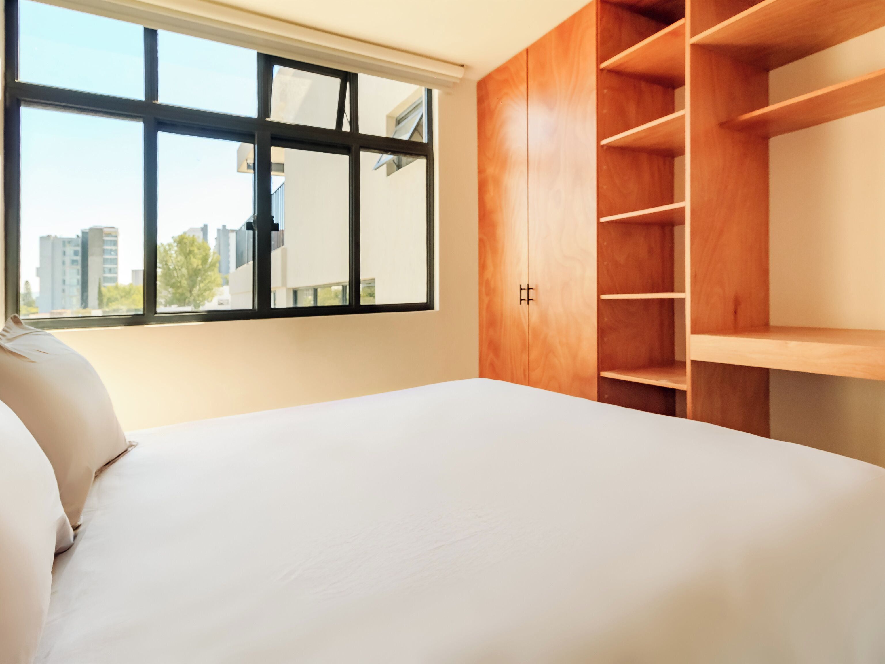 A bedroom with a large window, a bed, and wooden built-in shelving.