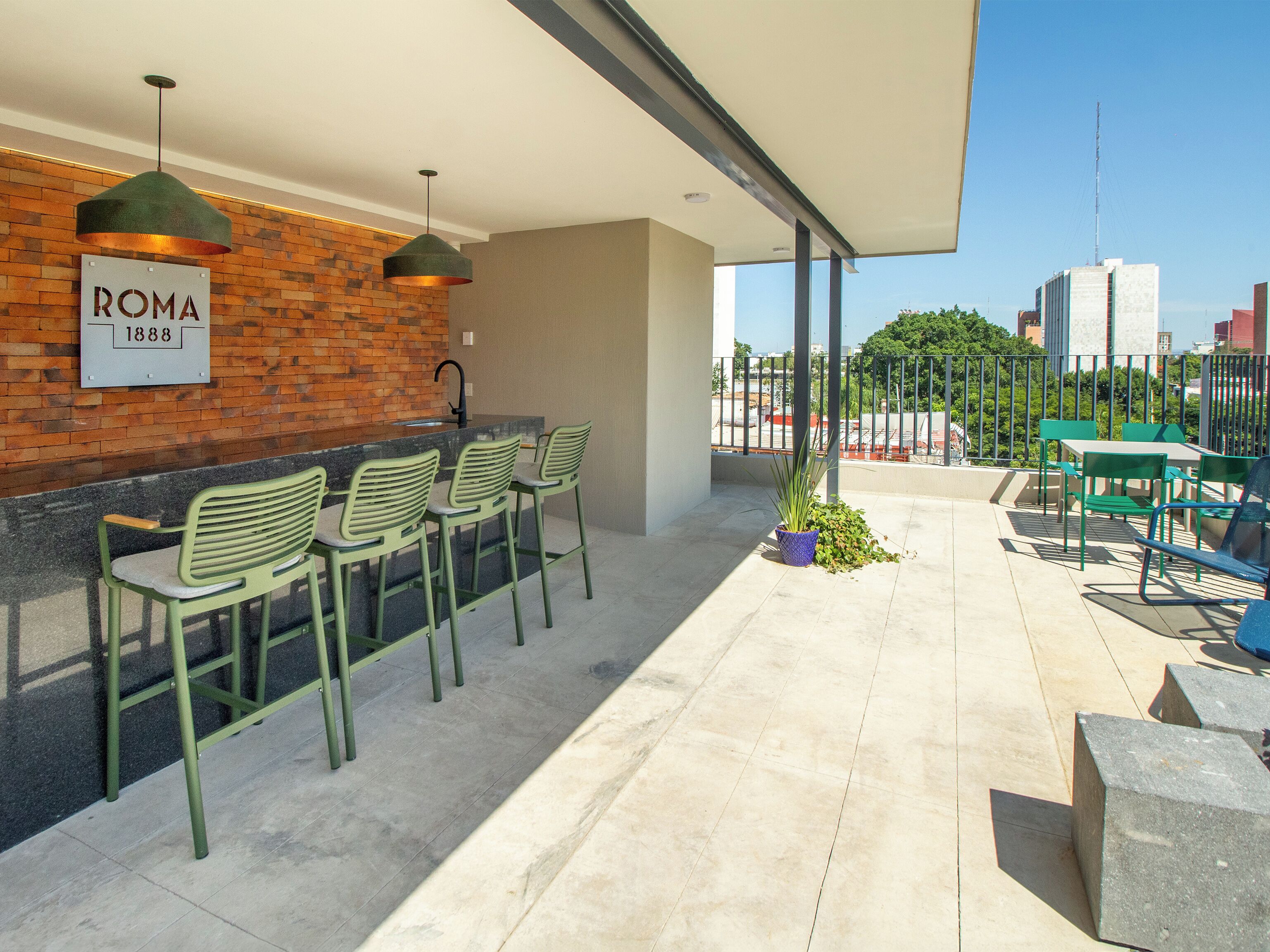 Un área de bar al aire libre con pared de ladrillo, sillas verdes y vista al horizonte de la ciudad.