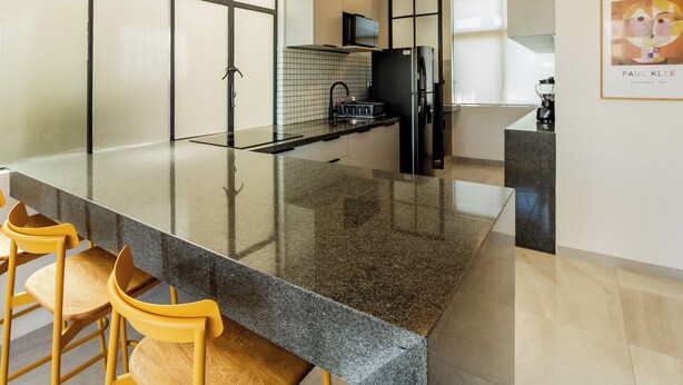 Eine moderne Küche mit einer großen Granitinsel, gelben Stühlen und einem schwarzen Kühlschrank.