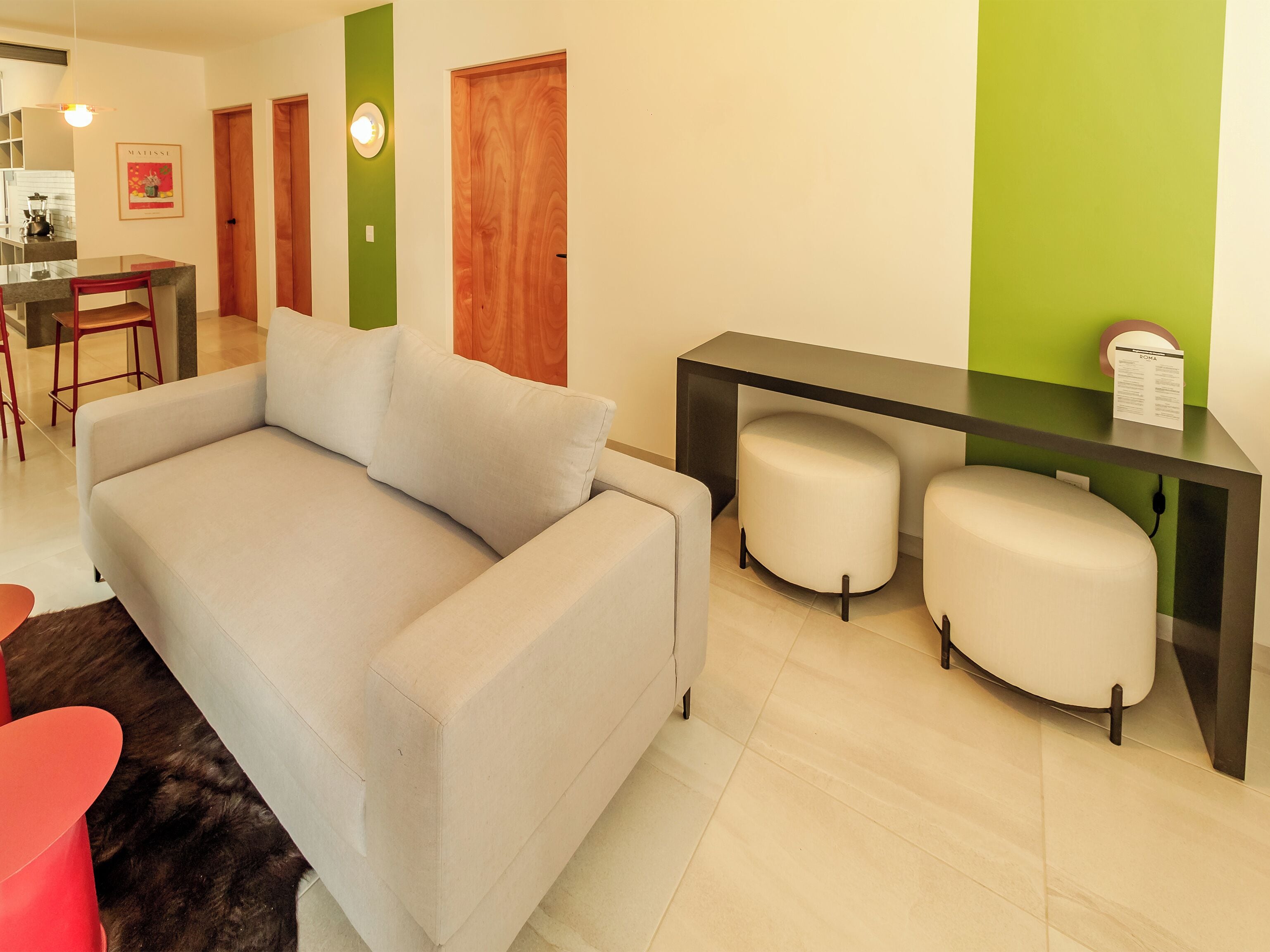 Una sala de estar moderna con un sofá gris, un pequeño comedor con una silla roja y una pared verde de acento.